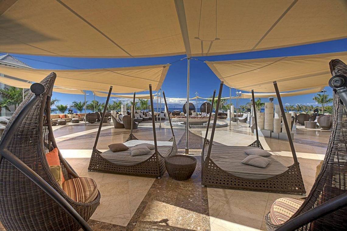 Gran Melia Palacio de Isora Loungebereich mit hängenden Sonnenschirmen und Liegen.