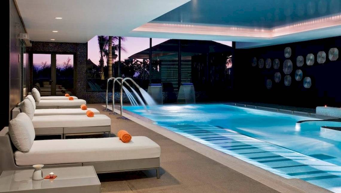 Innenpool-Lounge des Gran Melia Palacio de Isora mit weißen Liegen und Wasserfontäne.