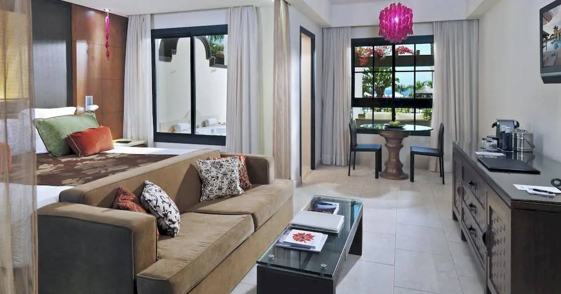 Innenansicht einer Hotelsuite im Gran Melia Palacio de Isora mit großem Bett, Sofa, Tisch, und Fenstern.