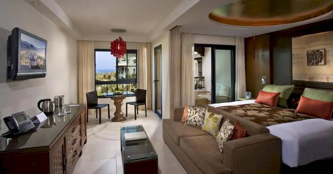 Innenansicht einer Suite im Gran Melia Palacio de Isora Hotel mit Bett, Couch, Tisch und Fernseher.