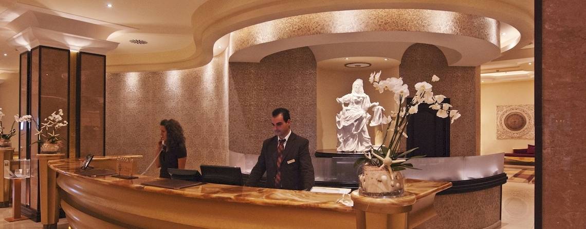 Rezeption des La Marquise Luxury Resort Complex mit einem Mann und einer Frau, Statue und Blumen im Hintergrund.