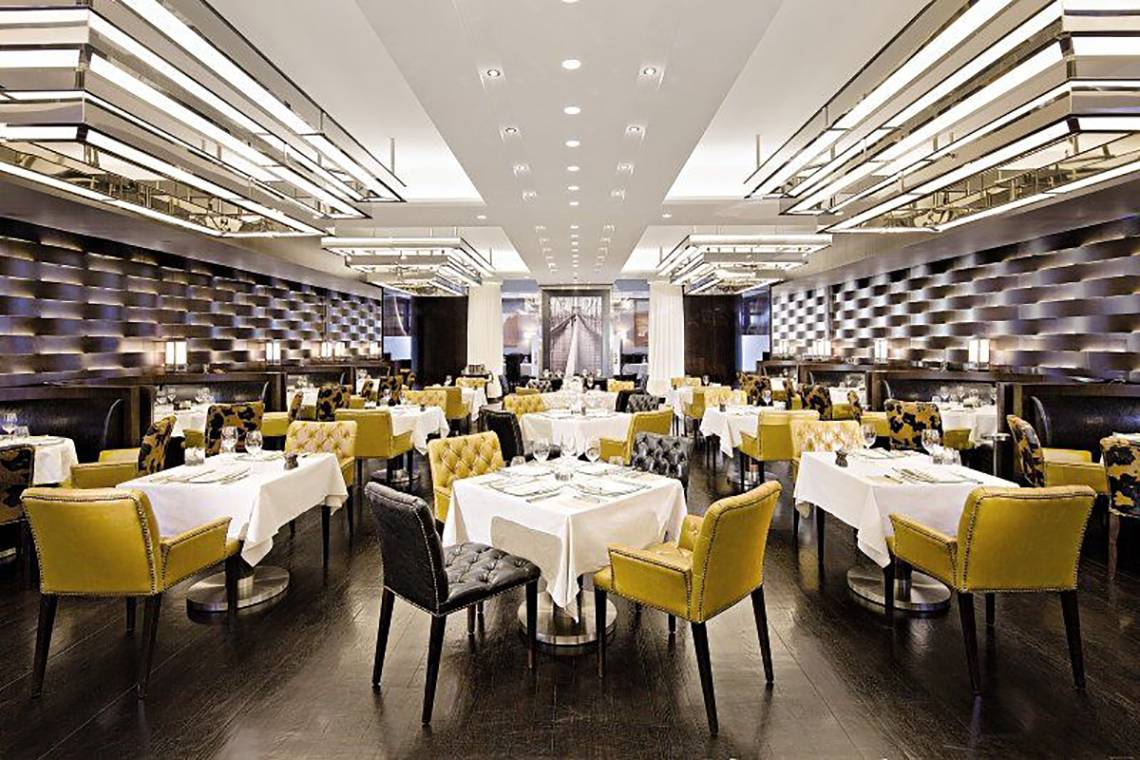 Innenansicht eines Restaurants im Jumeirah Emirates Towers mit gelben und schwarzen Stühlen und weißen Tischen.