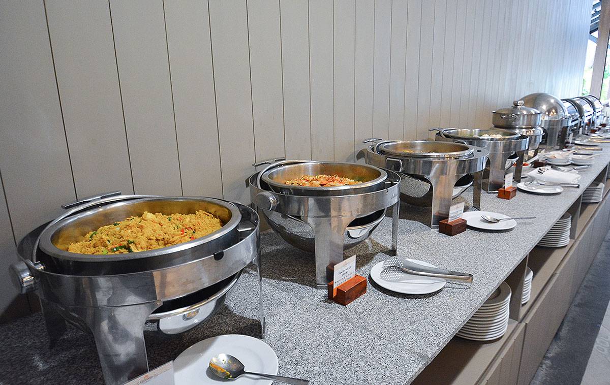 Buffet-Tisch im Andaman Cannacia Resort mit verschiedenen Gerichten in Silberschüsseln und leeren Tellern.