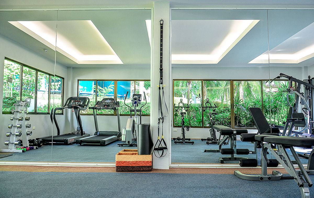 Fitnesscenter im Andaman Cannacia Resort mit Spiegeln, Laufbändern und Fenstern.
