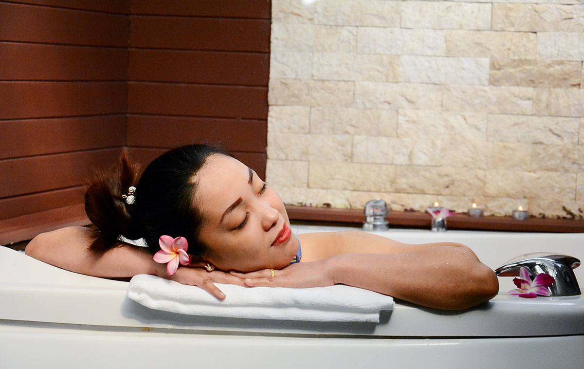 Frau im Badewanne mit Blumen im Andaman Cannacia Resort