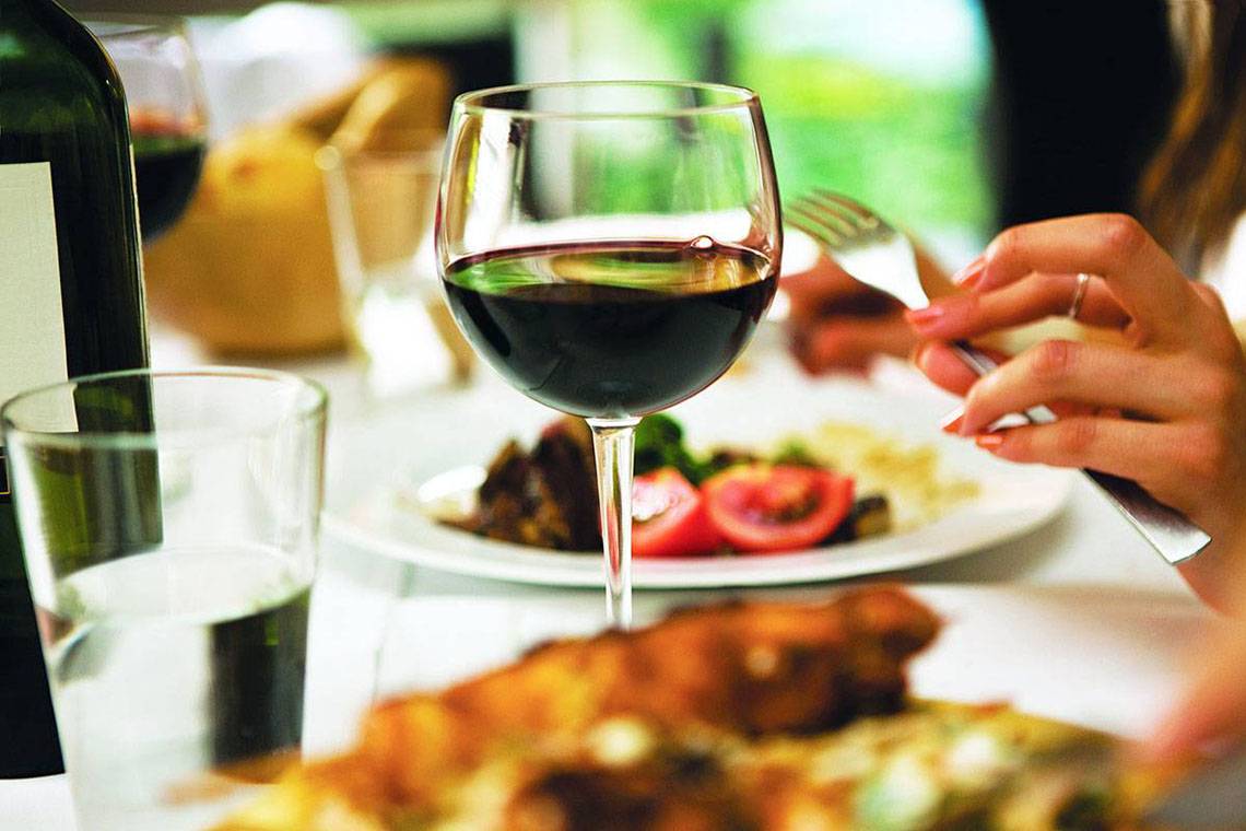 Eine Frau isst ein Essen und trinkt ein Glas Rotwein.