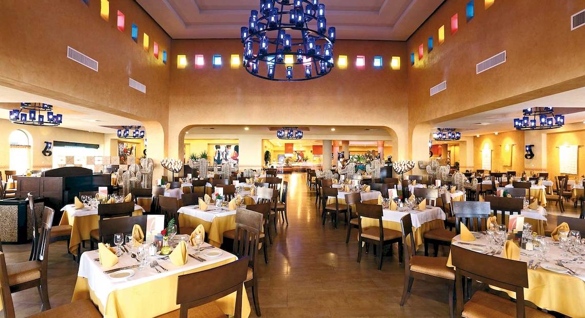 Restaurant des Barcelo Maya Palace Hotels mit vielen gedeckten Tischen und bunten Kronleuchtern.