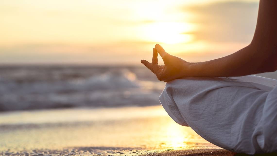 Person in Yoga Meditation am Strand bei Sonnenuntergang