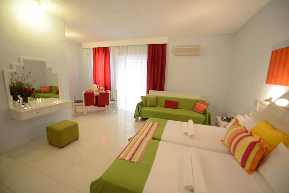 Innenansicht eines Zimmers im Golden Star Hotel auf Kos mit zwei Betten, grünen Kissen und einem grünen Sofa.