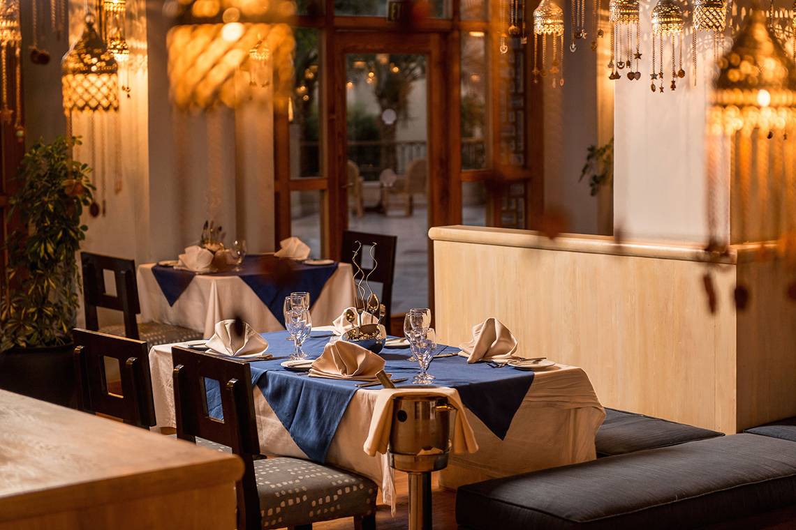 Restauranttisch mit blauer Tischdecke, Servietten und Gläsern, goldene Kronleuchter im Hintergrund.