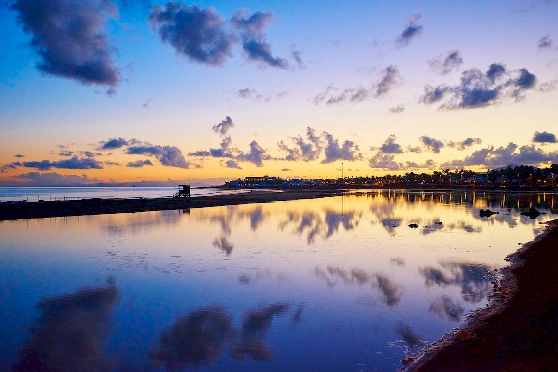 Sonnenuntergang am Strand vor Hipotels La Geria mit Wasserreflexionen und blauem Himmel