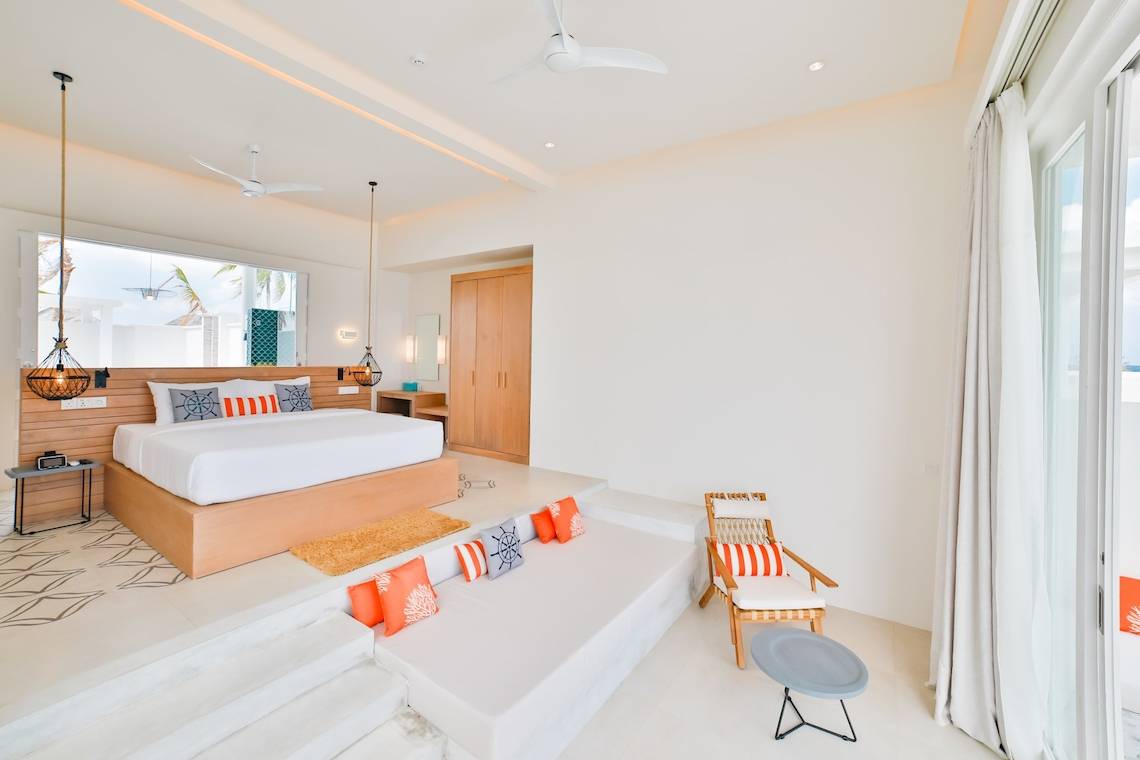 Modernes Zimmer im Sun Siyam Iru Veli Hotel mit großem Bett, Kissen und Holzmöbeln.