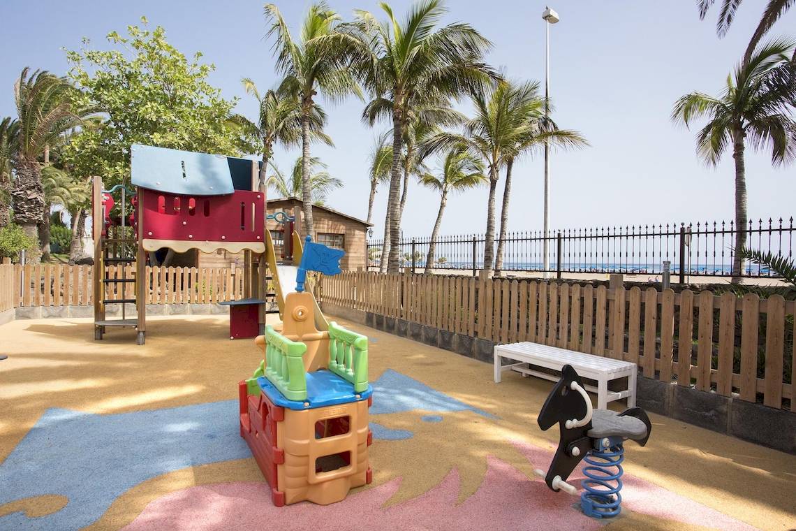 Spielplatz im Hipotels La Geria mit bunten Spielgeräten und einem Blick auf den Strand.