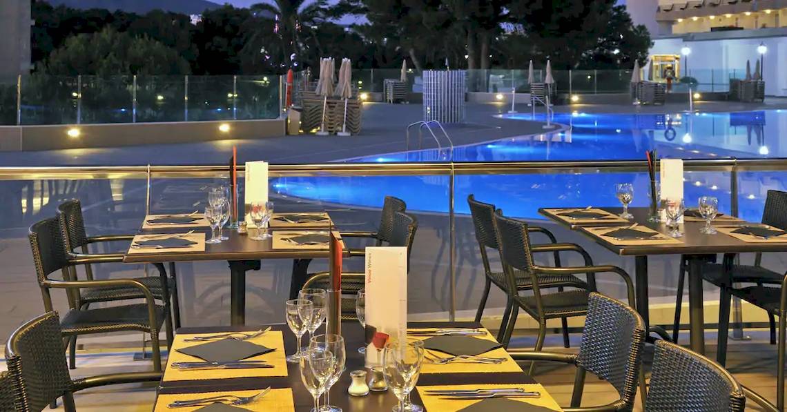 Außenbereich des Sol Barbados Hotels mit beleuchtetem Swimmingpool und gedeckten Tischen.