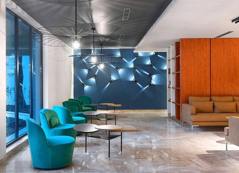 Lobby des HVD Club Bor Hotels mit blauen und grünen Stühlen, runden Tischen und einem großen Sofa.