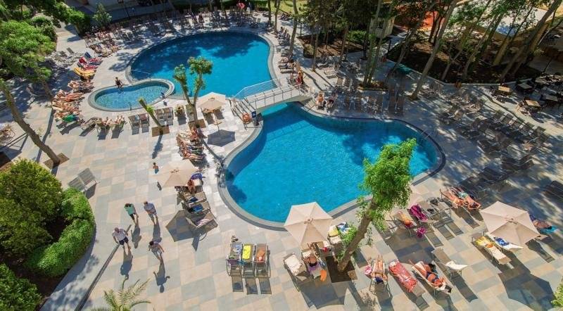 Luftaufnahme des Außenpools des HVD Club Bor Hotels mit vielen Gästen und Sonnenschirmen.