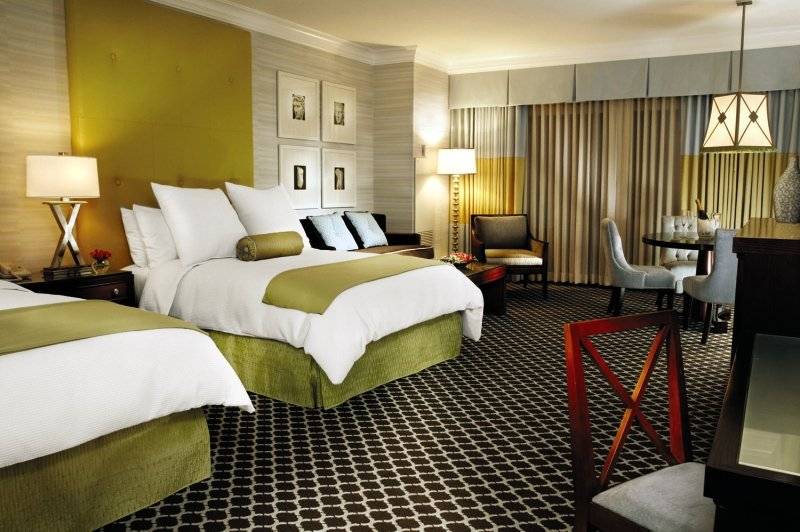 Doppelbett-Zimmer im Caesars Palace mit grünen und weißen Kissen, zwei Lampen und Möbeln.
