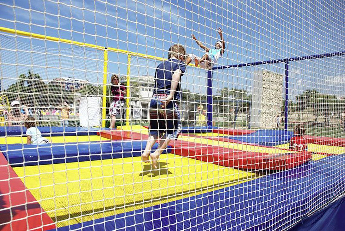 Kinder springen auf Trampoline in einem abgesperrten Bereich draußen.