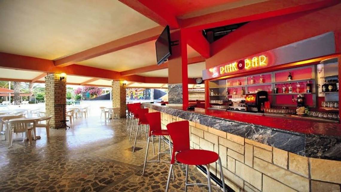 Innenansicht der Bar im Miramare Beach Hotel mit roten Stühlen und einer Theke.