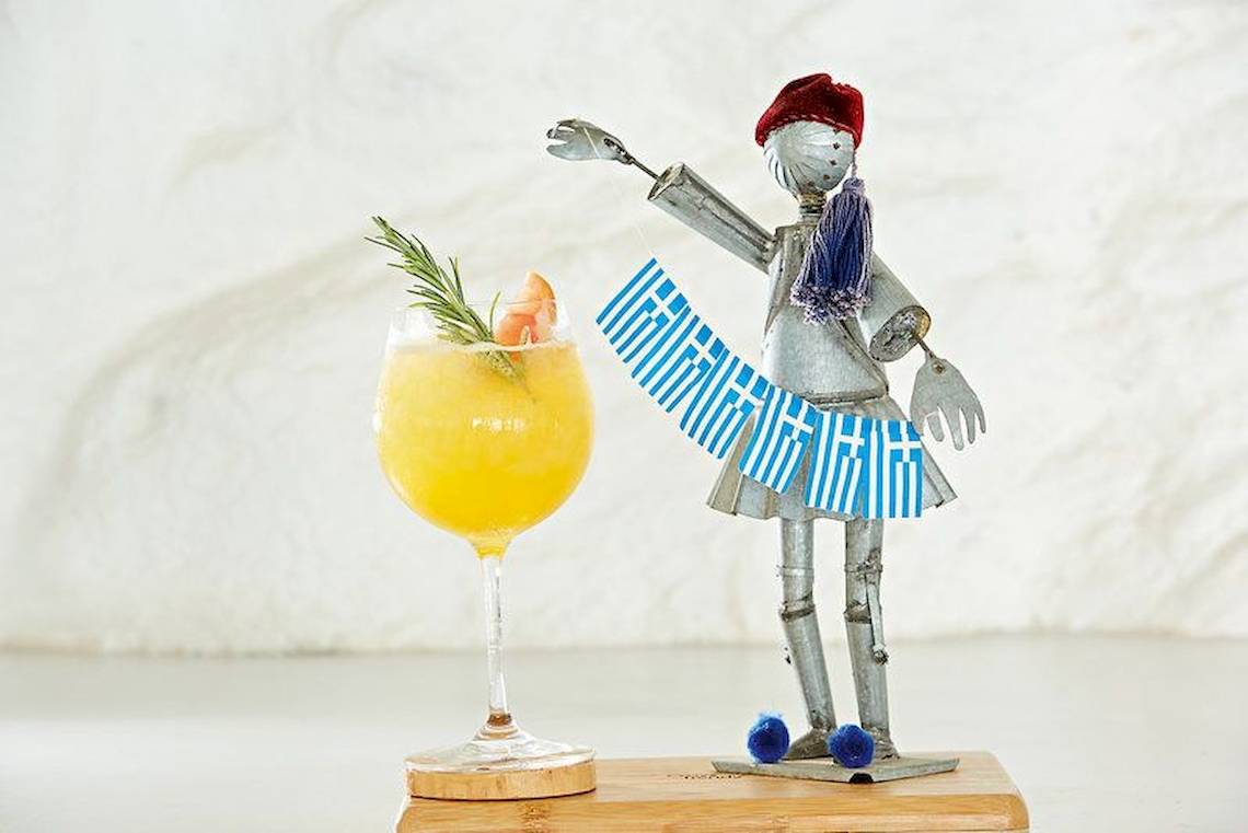 Ein Getränk in einem Glas mit griechischem Motiv neben einer Statue