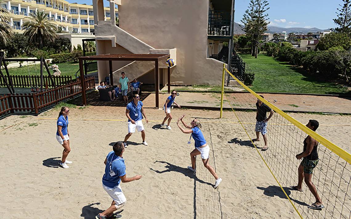 Mehrere Personen spielen Volleyball auf dem Sandplatz des Aphrodite Beach Clubs.