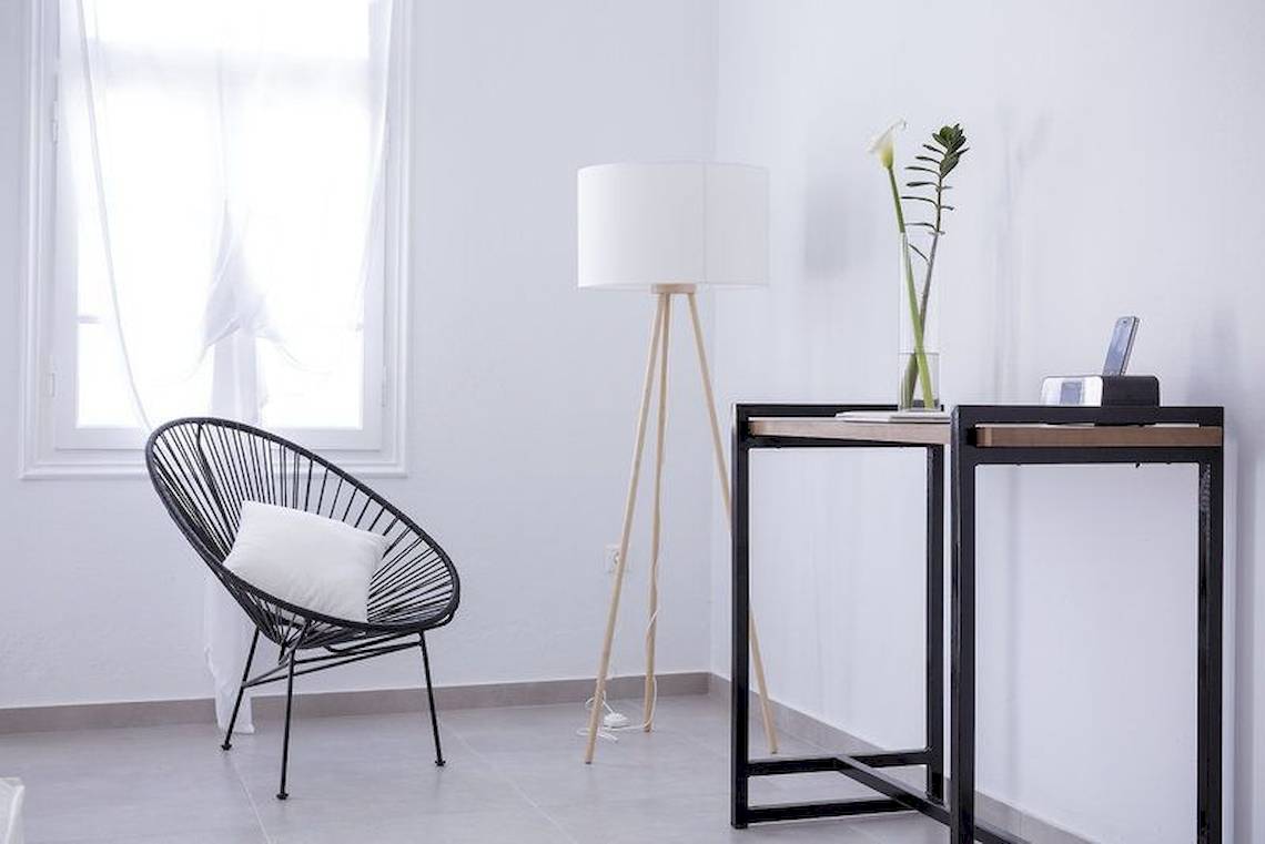 Innenraum des Pietra E Mare Mykonos Hotels mit einem schwarzen Stuhl, einer Stehlampe und einem Tisch mit einer Pflanze.