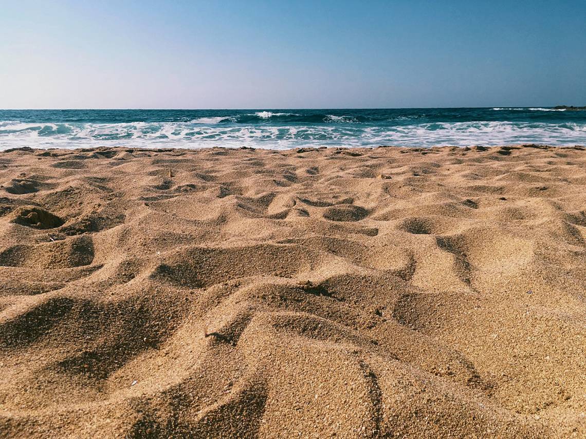 Strand mit feinem Sand und dem Meer im Hintergrund, wo Wellen sanft an die Küste stoßen.