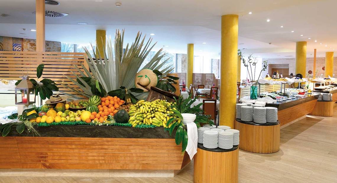 Buffetbereich im Barcelo Fuerteventura Mar Hotel mit vielen Früchten und gestapelten Tellern.