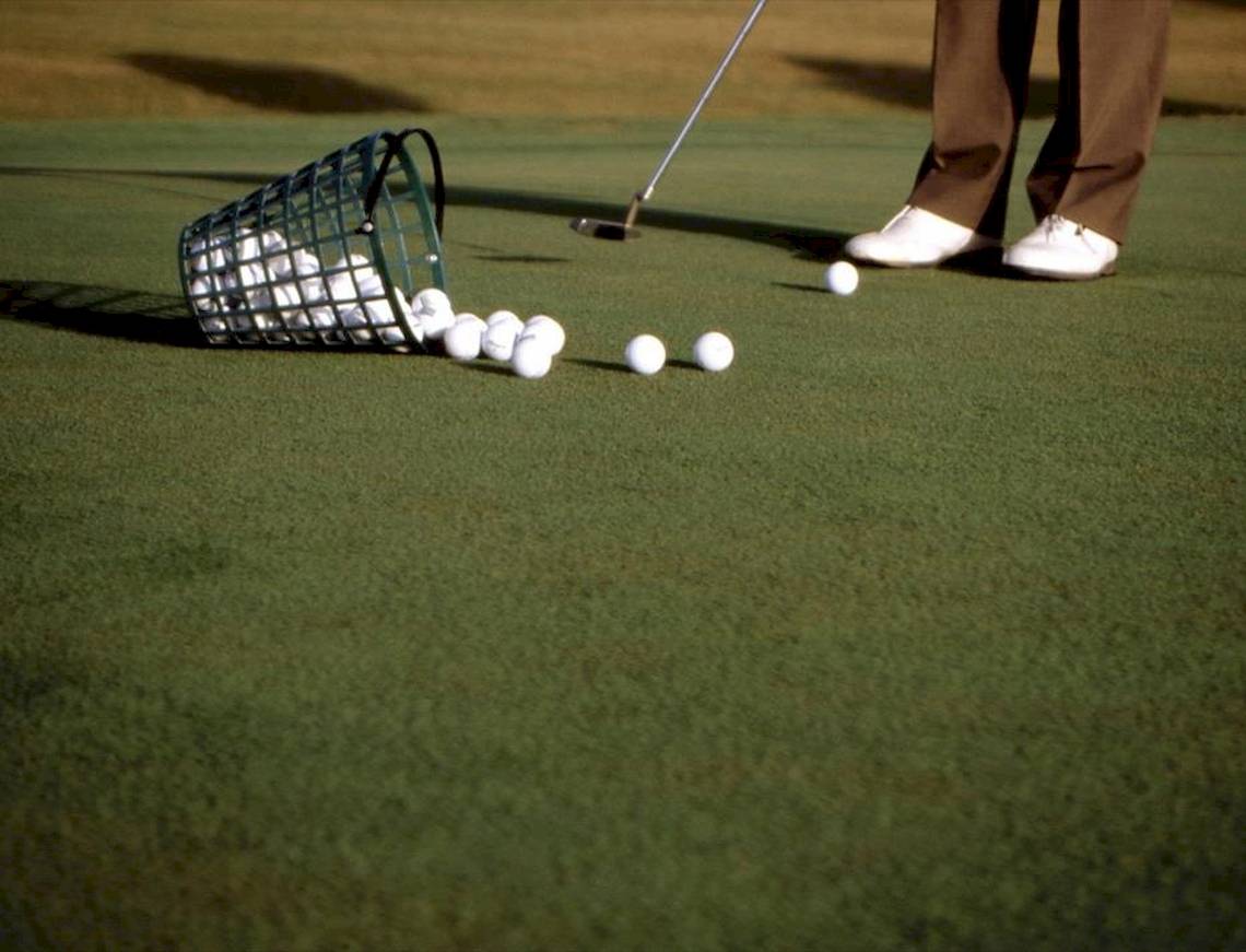 Golfplatz mit Golfer, Golfschläger, Golfbällen und Golfkorb.