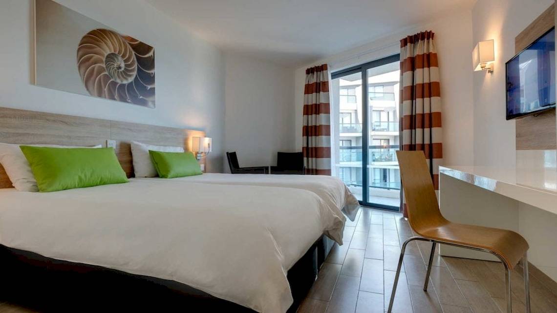 Doppelzimmer im Seashells Resort at Suncrest mit zwei Betten, grünen Kissen und einem offenen Balkon.