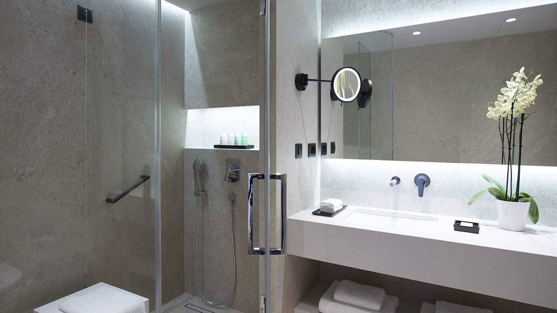 Badezimmer im Neptune Luxury Resort mit Glasdusche, Waschbecken, Spiegel und Blumenvase