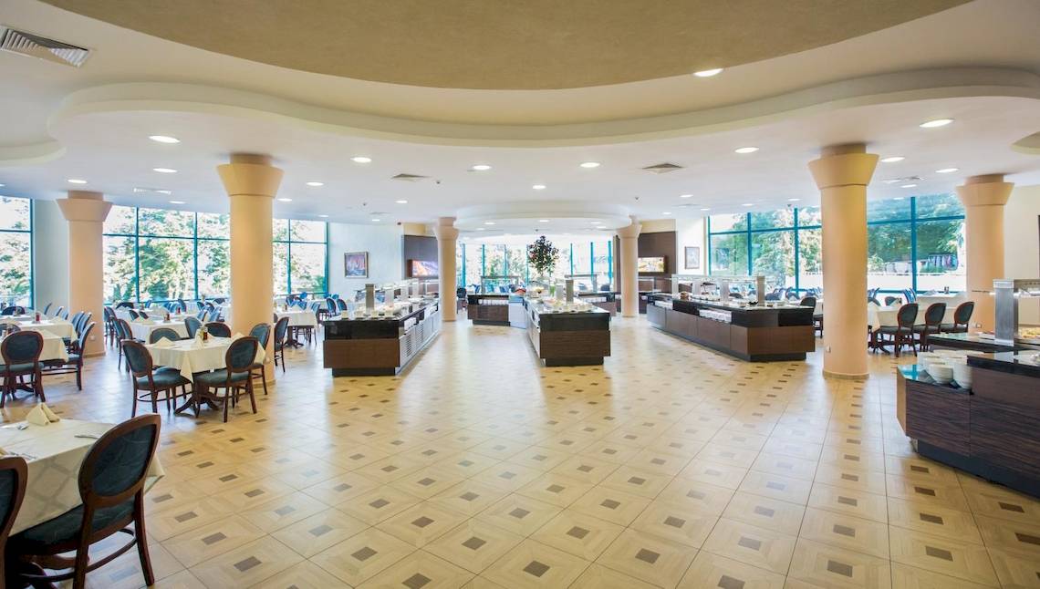 Innenbereich des Marina Grand Beach Hotels mit vielen Tischen und Stühlen, Buffettischen und großen Fenstern.