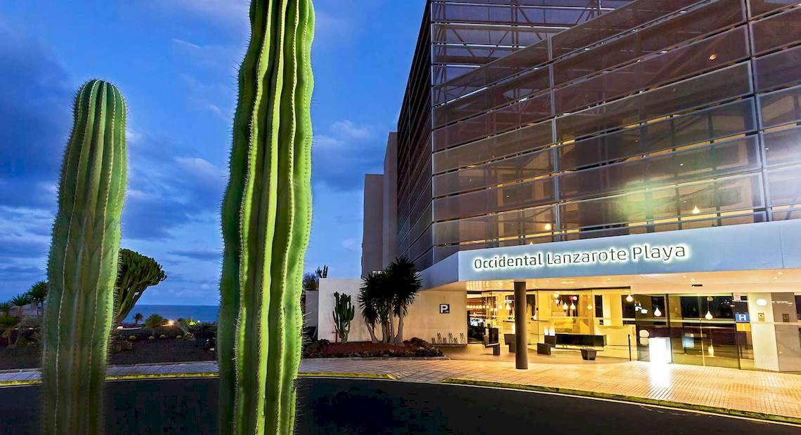 Vorderansicht des Barcelo Lanzarote Active Resort mit Kakteen vor dem Gebäude und Meer im Hintergrund