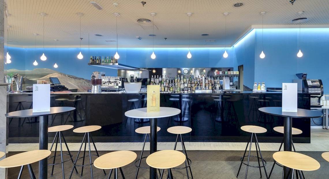 Bar im Barcelo Lanzarote Active Resort Hotel mit Barhockern, Tischen und einer Bar im Hintergrund.