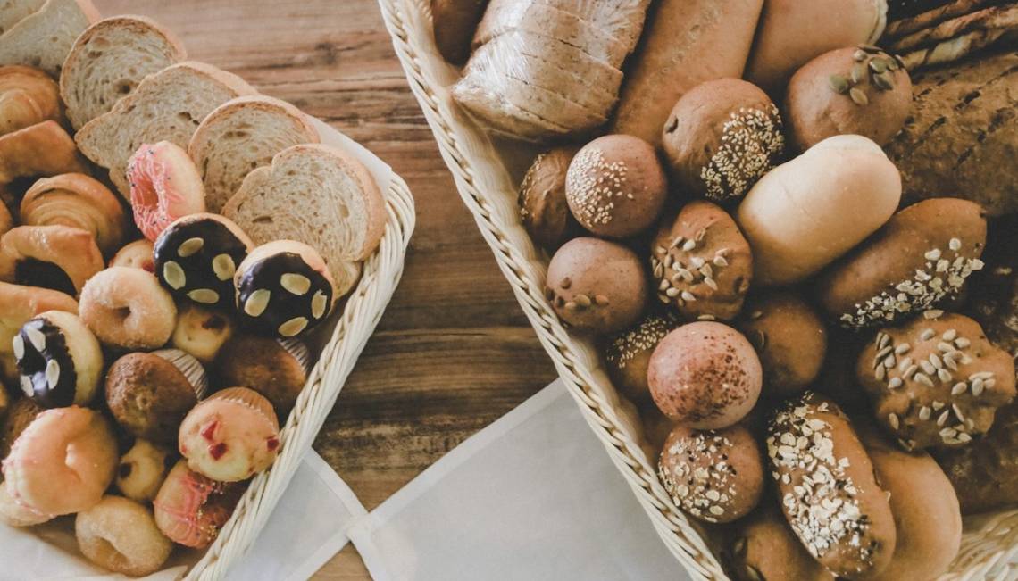 Zwei Körbe mit verschiedenen Gebäckstücken und Broten auf einem braunen Tisch