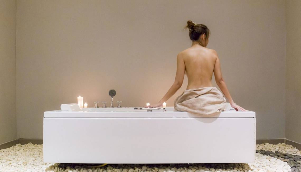Frau sitzt nackt auf einer weißen Badewanne mit Kerzen im Beyond Resort Krabi.