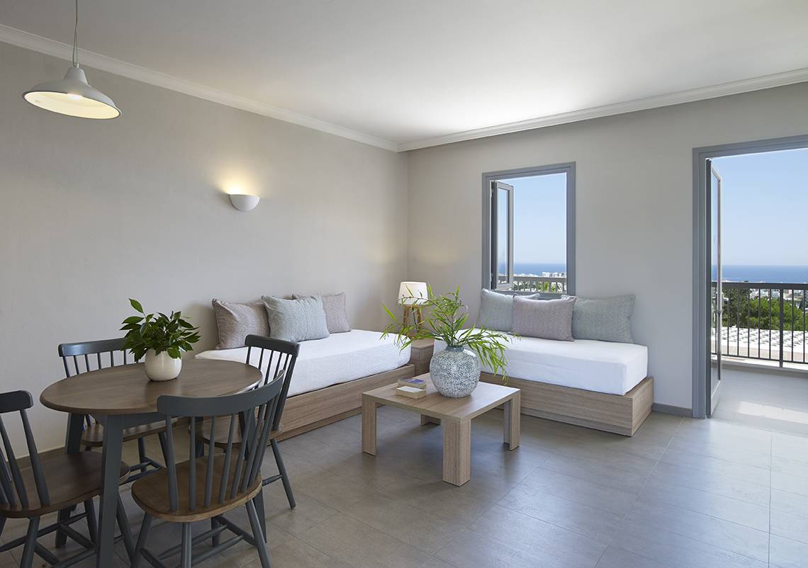 Innenansicht einer Suite im Louis St. Elias Resort & Waterpark mit zwei Betten, Tisch, Stühlen und Ausblick auf das Meer.