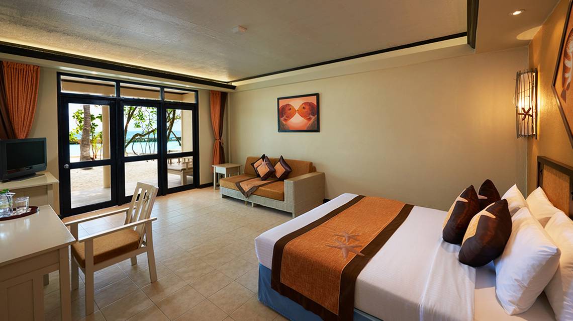 Innenansicht eines Zimmers im Ellaidhoo Maldives by Cinnamon mit Meerblick, Doppelbett, Wohnzimmerbereich und Fernseher.