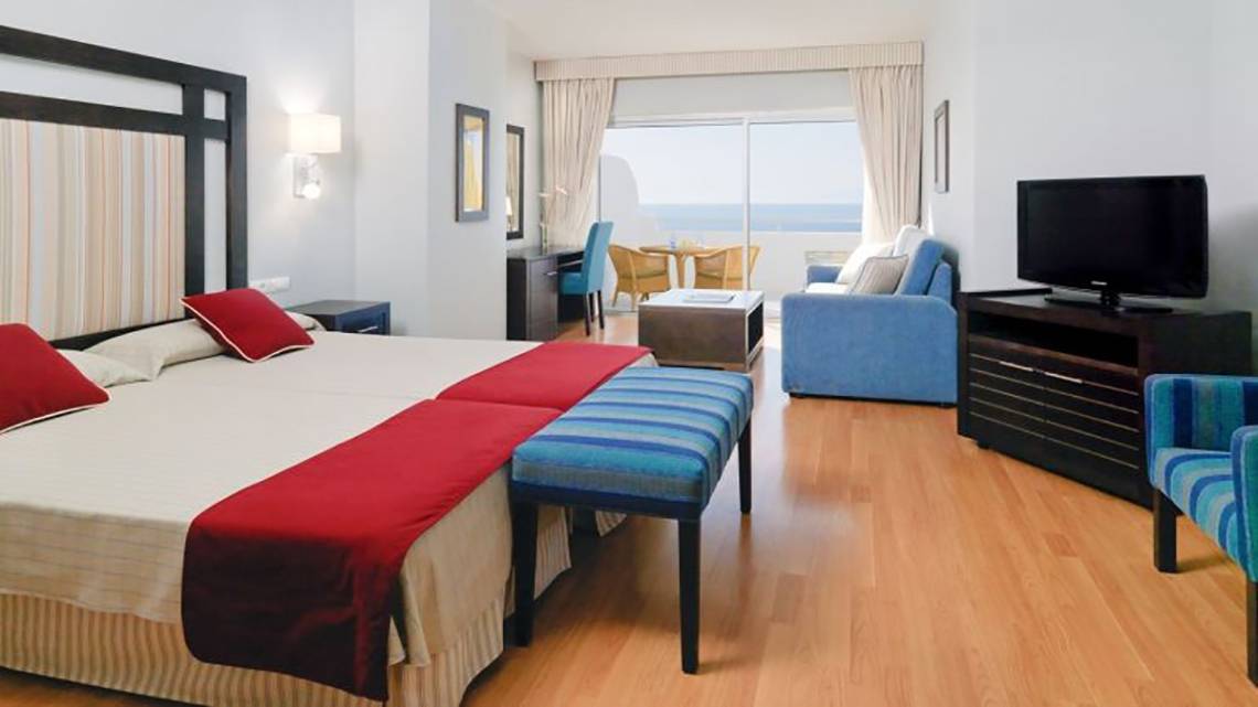Hotelzimmer im H10 Gran Tinerfe mit zwei Betten, einem Fernseher, einem Schreibtisch und einem Balkon.
