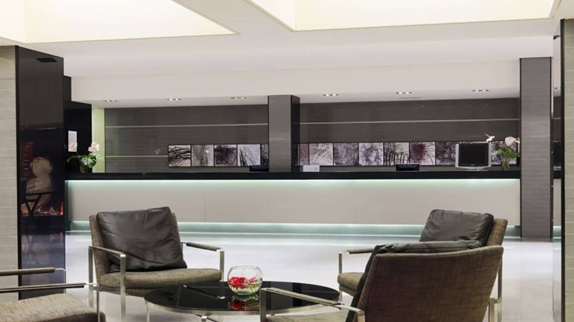 Lobby-Lounge-Bereich des H10 Gran Tinerfe Hotels mit Sitzmöbeln, Empfangstresen und zentralem Tisch.