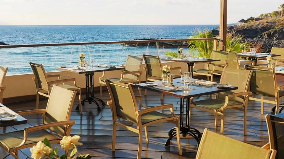 Außenterrasse des H10 Gran Tinerfe Hotels mit Blick auf das Meer und arrangierten Tischen und Stühlen.