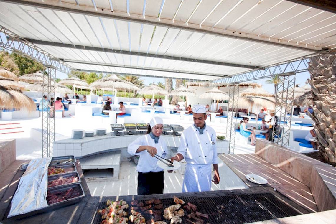 Zwei Köche bereiten Speisen auf einem Grill im Freien im El Mouradi Djerba Menzel Hotel zu.
