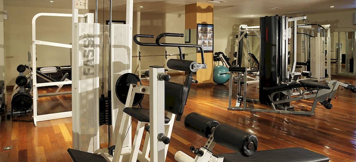 Fitnessstudio im Victoria Beachcomber Resort & Spa mit verschiedenen Trainingsgeräten auf einem hölzernen Boden.