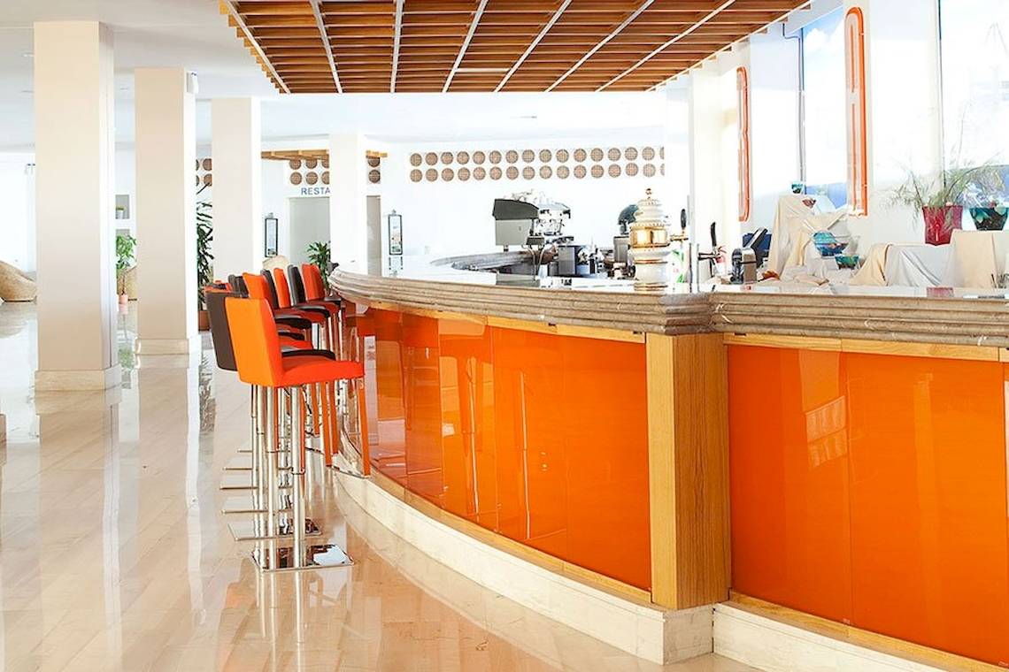 Innenansicht der Bar im Lindos Bay Hotel mit orangefarbenen Stühlen und Theke.