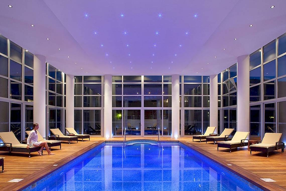 Ein Innenpool im Lindos Bay Hotel mit Lounge-Sesseln und einer Frau, die entspannt sitzt.