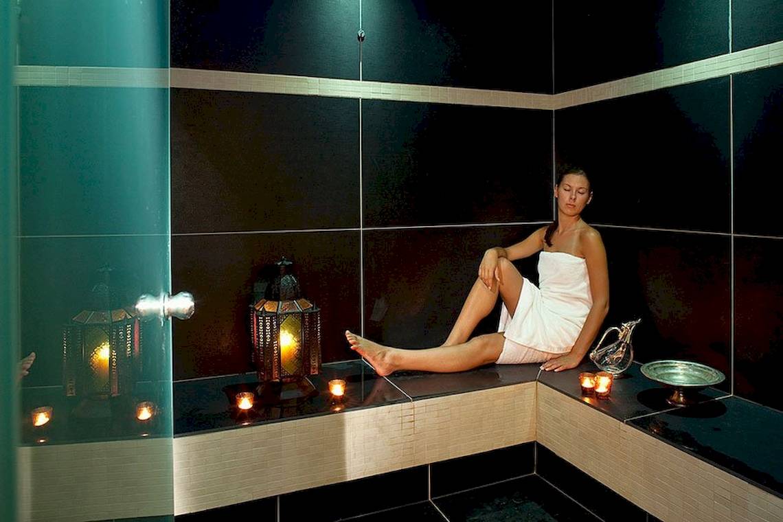 Eine Frau sitzt in einer Sauna im Lindos Bay Hotel, mit Kerzen und Dekor.