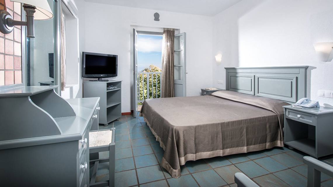 Ein Schlafzimmer im Silva Beach Hotel mit Fernseher, Bett, Nachttischen und einem Balkon.
