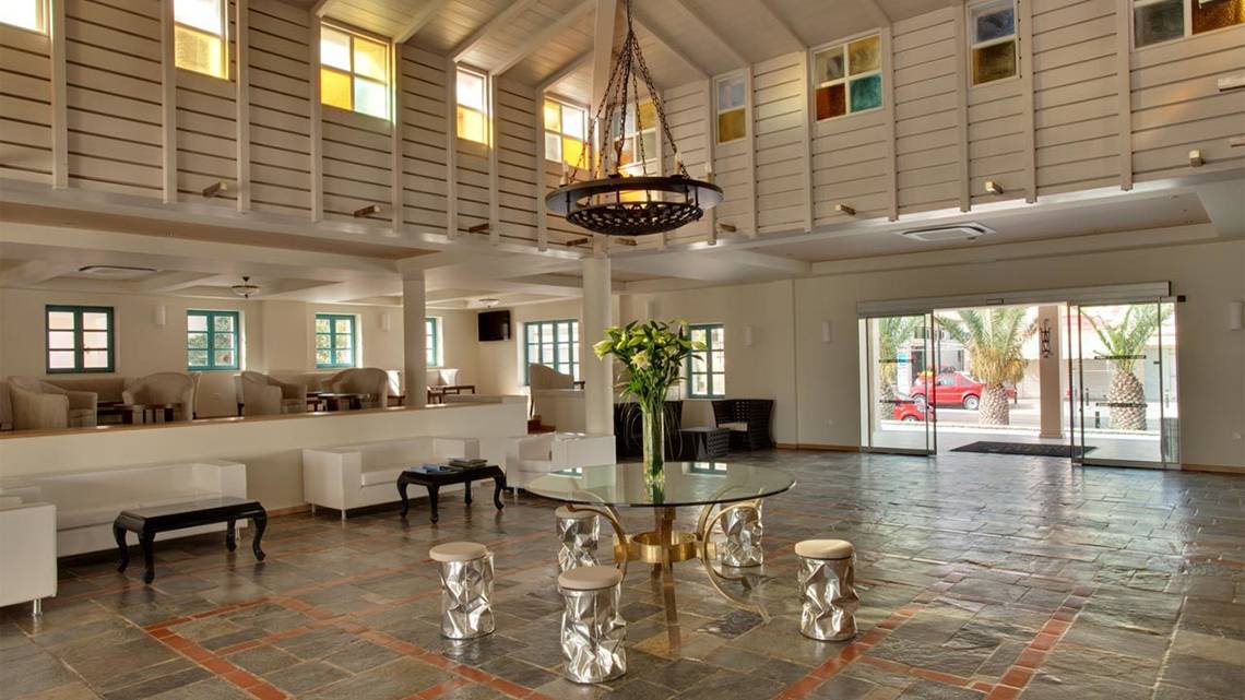 Lobby im Silva Beach Hotel mit einem großen Glastisch, Blumenvase, und weißen Möbeln.