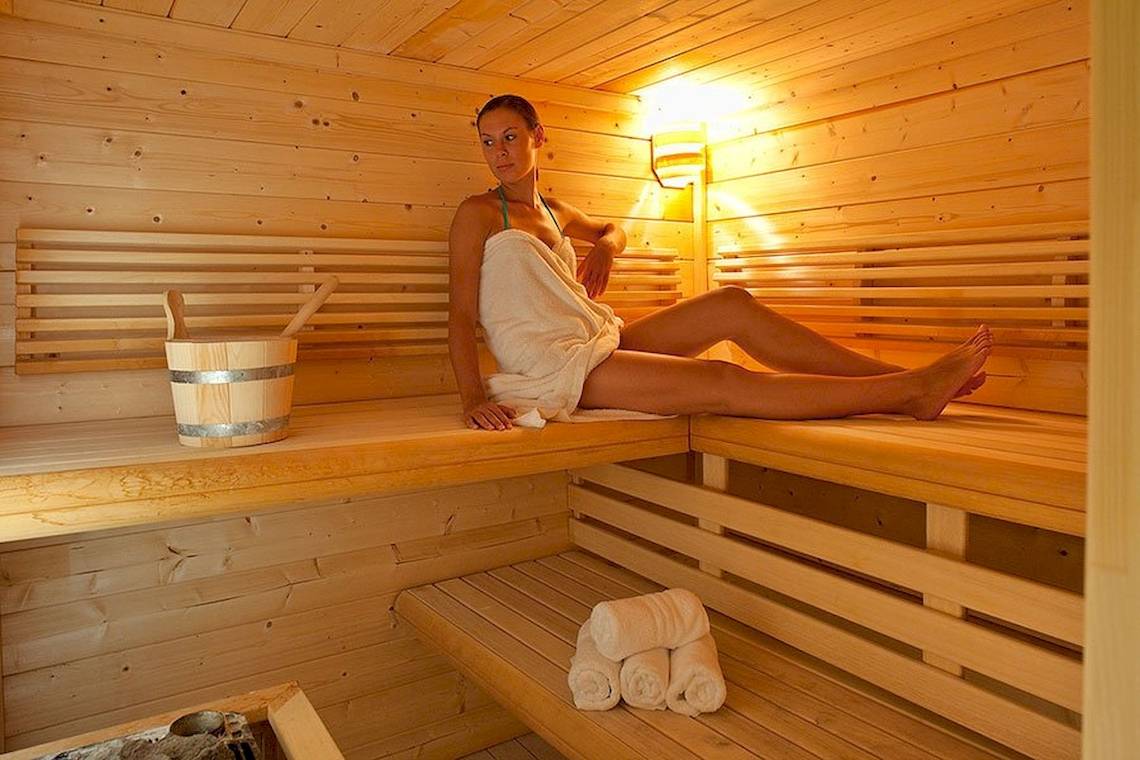 Eine Frau in einem weißen Handtuch sitzt in einer Holzsauna im Lindos Bay Hotel.