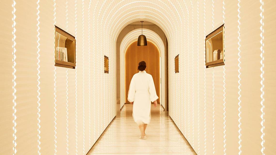 Eine Frau in einem weißen Bademantel geht durch den Eingang des Spas im Raffles The Palm Dubai.